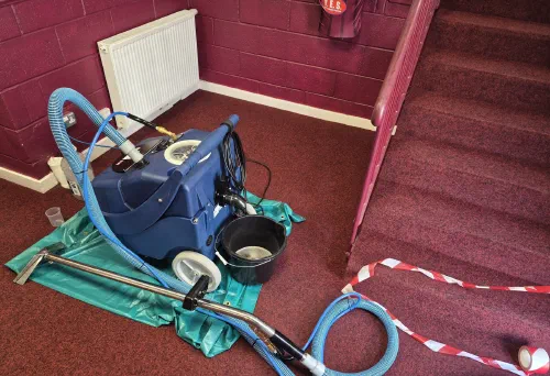 A portable carpet cleaning machine on a sheeted floor, hoses run out across the carpet and the stairs taped off.
