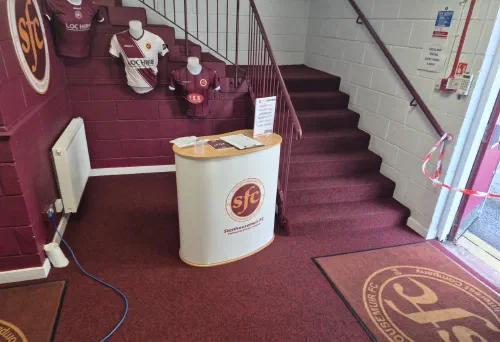 The reception at Ochilview Park, with the Stenhousemuir FC desk and the club crest on the floor mat.